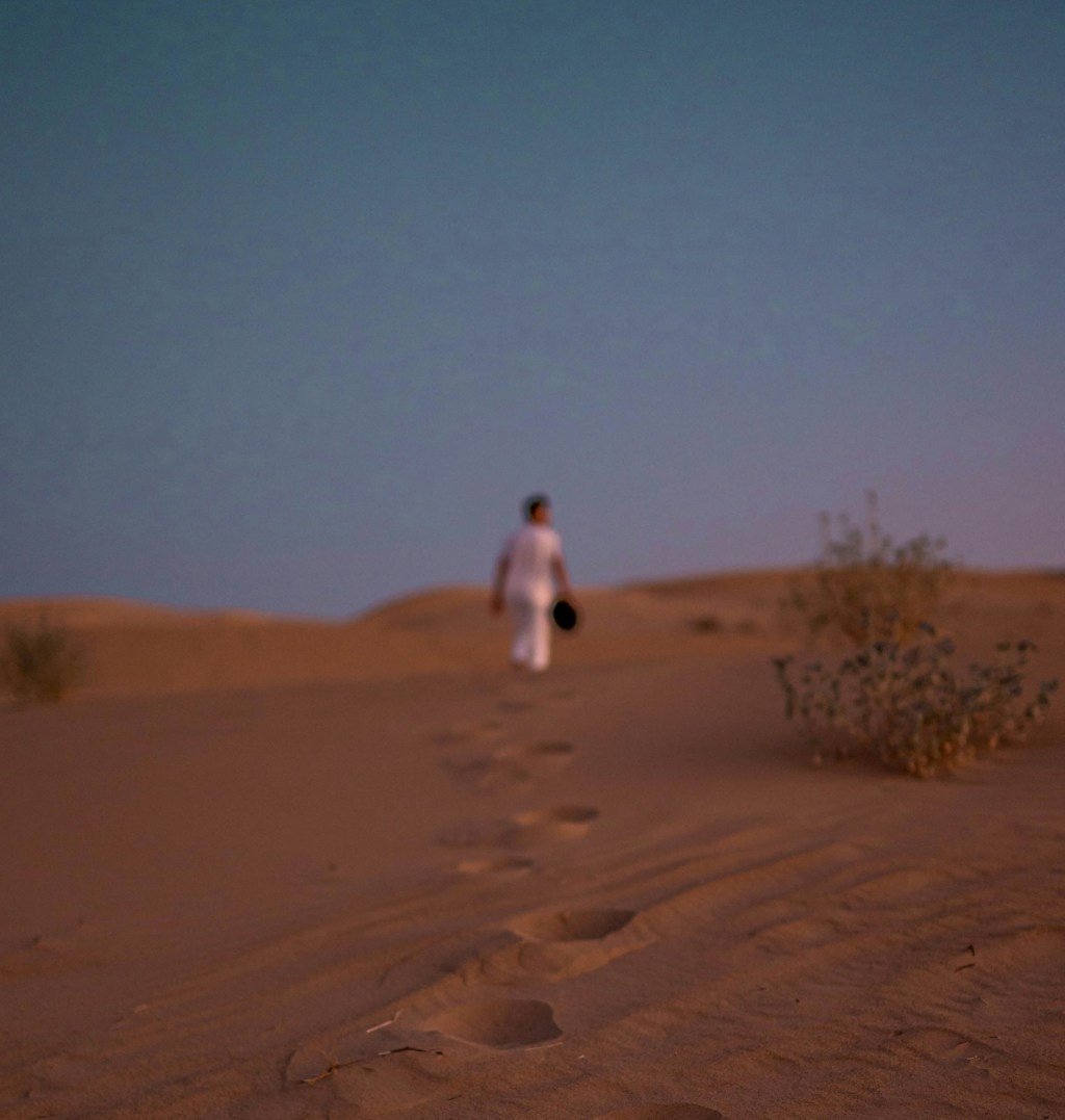 Footsteps in the sand on a beach, man walking in the distance.